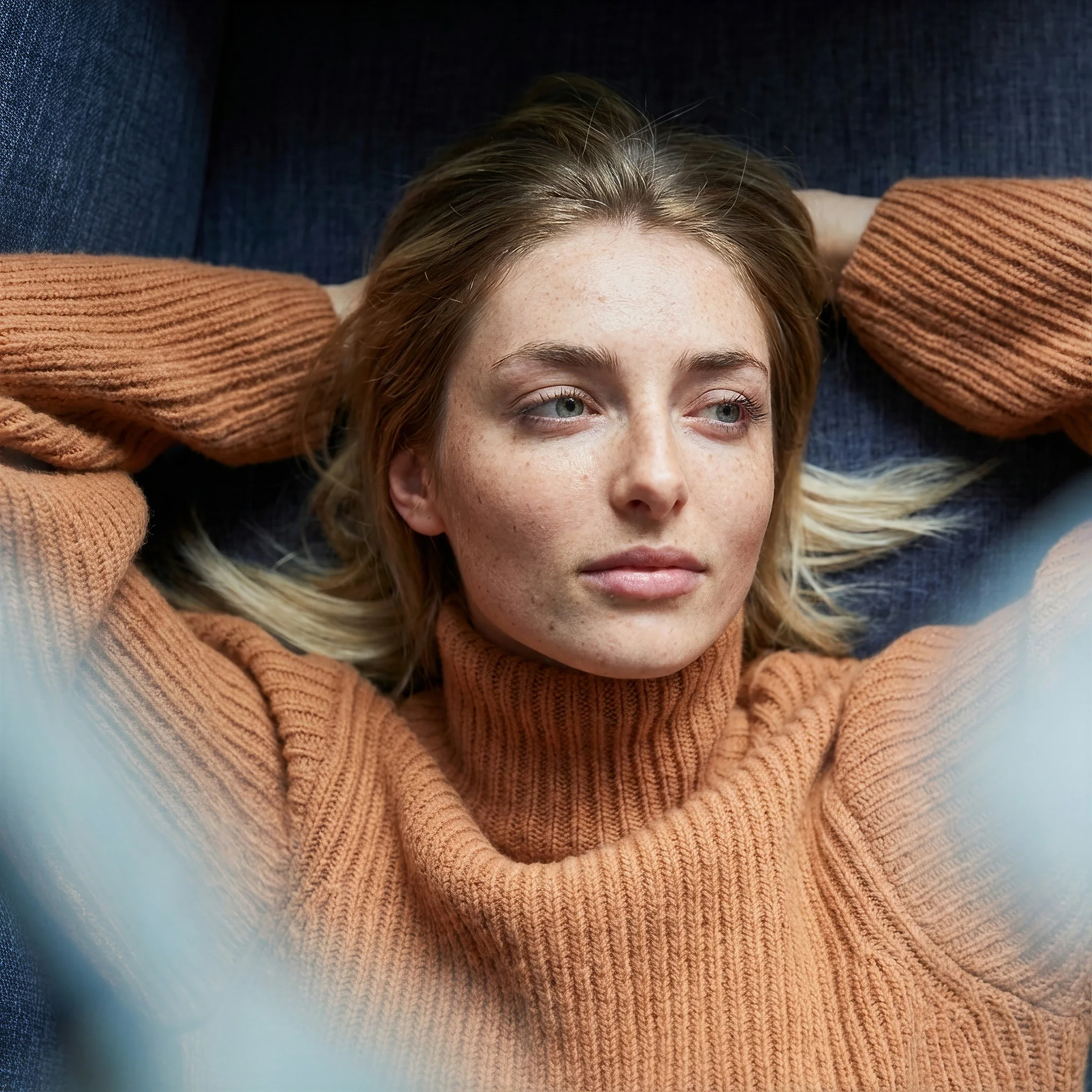 A young woman in an orange knit sweater lying back with her hands behind her head